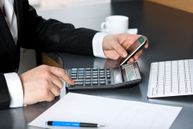 Photo of person at desk with phone, calculator, keyboard, and documents